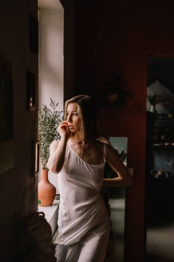 Açık renk gecelikli yetenekli heykeltraş kız geniş pencerenin yanındaki çömlekçilik atölyesinde duruyor. konsept güzellik