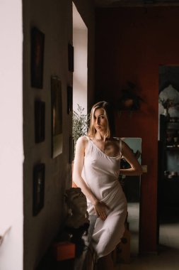 Açık renk gecelikli yetenekli heykeltraş kız geniş pencerenin yanındaki çömlekçilik atölyesinde duruyor. konsept güzellik