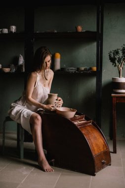 İnce ışıklı sabahlık giyen yetenekli heykeltraş kız geniş pencerenin yakınındaki çömlekçilik atölyesinde kilden bir sürahi heykel yapıyor. Heykel kavramı