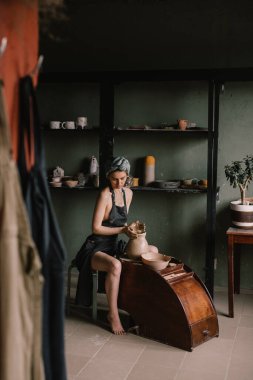 Genç heykeltıraş, kafasında bandajlı ve siyah önlüklü bir kız, çömlekçilik atölyesinde büyük pencerenin yanındaki kil ürünü yontuyor. Kavram hobidir.