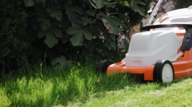 Arka bahçedeki çimleri elektrikli çim biçme makinesiyle biçen adamı yakından çek.