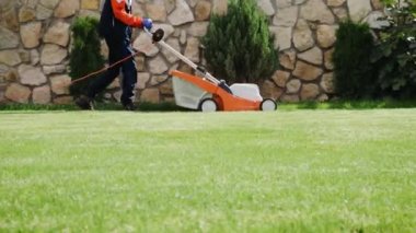 Çim biçme makinesi çimleri kesiyor. Bahçe işleri. Güneşli bahçede çim biçme makinesiyle çim biçmek. Bahçede çim biçme makinesiyle çalışan bahçıvan. Çim biçme makinesi yeşil çimleri kesiyor