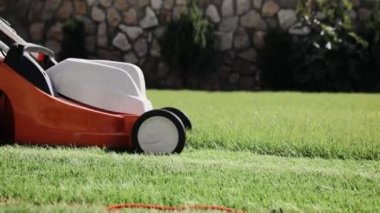 Bir adam elektrikli çim biçme makinesiyle arka bahçedeki çimleri biçiyor. Yavaş çekim, çim biçerken yakın çekim.