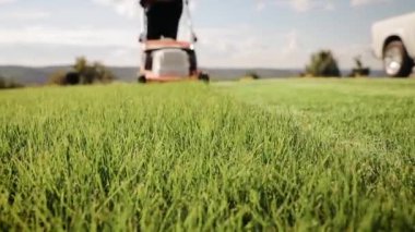 Bahçede yeşil çimenler ve arka planda çim biçme makinesi olan bir adam yaklaşıyor. Yavaş çekim, çim biçerken yakın çekim.