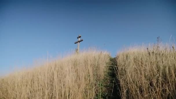 Alguien con una cámara sube una colina en la que se levanta una cruz de madera — Vídeo de stock