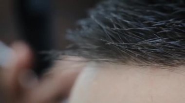 Genç yetişkin bir adam saçlarını tarıyor bir tarakla. Berber adam berber dükkanında bir tutam müşteriyi tarar. Makro video