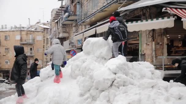 Kinderen spelen op een grote berg sneeuw na een sneeuwval bij de Machaneh Yehudah Markt in Jeruzalem, Israël, januari 2022 — Stockvideo