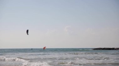 Kimliği belirsiz insanlar denizde uçurtma gibi uçuyor. Ocak 2022 'de Tel Aviv sahilinde çok renkli uçurtmalar sörf ve mavi gökyüzü.