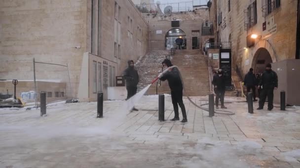 Trabajador quitando nieve helada con una manguera de hidrante de agua de la acera después de la nevada en la Ciudad Vieja de Jerusalén, Israel, Enero 2022 — Vídeo de stock