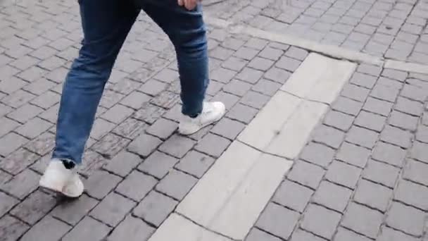Primer plano de seguimiento de las piernas de un hombre en zapatillas blancas y un vaquero caminando con confianza hacia adelante en la acera en la calle Tel Aviv. 50 FPS para cámara lenta — Vídeos de Stock