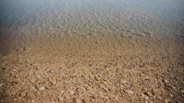 Ölü Deniz 'de temiz su, burada kumlu tabanı ve küçük taşları görebilirsiniz. Derinlerde tuzlu taşlarla kaplı