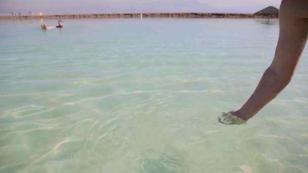 Mužská ruka se dotýká mořské vody. Žena plavající v pozadí. Mrtvé moře je jedním z nejslanějších přírodních útvarů na Zemi — Stock video