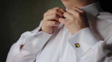 Close-up of person dressing white shirt. Cufflink emblem with pride rainbow flag. LGBT wedding preparation