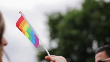 Unrecognisable woman holds and waving rainbow flag on the blurred background of participants crowd of LGBT pride parade. Symbol of lesbian gay bisexual and transgender rights love equality and freedom