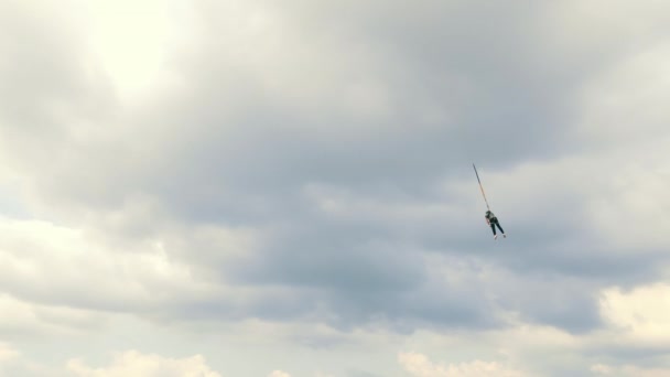 Arızalanmış ve bulutlu bir gökyüzüne karşı emniyet halatına tutunmuş bir dağcı. Tehlikeli bir dağcılık işi. Adam ayakkabı bağcığına asılmış.. — Stok video