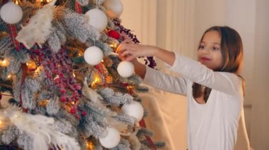Genç bir çocuk Noel ağacını süslüyor ve yılbaşını ve yılbaşını kutlamaya hazırlanıyor. Mutlu çocuk tek başına Noel ağacına süsleme yapıyor..