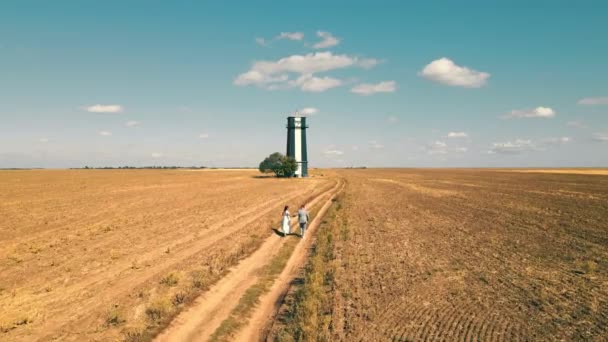 Einsamer Leuchtturm an einem sonnigen, hellen Tag auf dem Feld. Zwei Menschen halten sich an den Händen und rennen zum Leuchtturm — Stockvideo