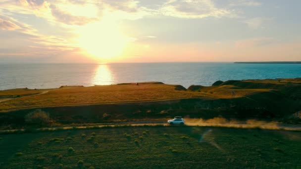 Viaje de carro pelo mar ao pôr-do-sol. Uma bela paisagem de um penhasco e um carro se movendo para atender o sol — Vídeo de Stock