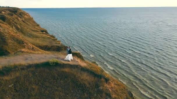 Luftaufnahme Ein paar Menschen stehen am Rande einer Klippe und beobachten den wunderschönen Sonnenuntergang am Meer. — Stockvideo