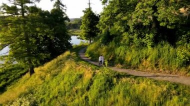 Gün batımında gölün yanındaki parkta yürüyen genç bir çift. Yeni evliler yeşil bir parkta yürüyorlar. Parkta kuş bakışı bir çiftin fotoğrafı.