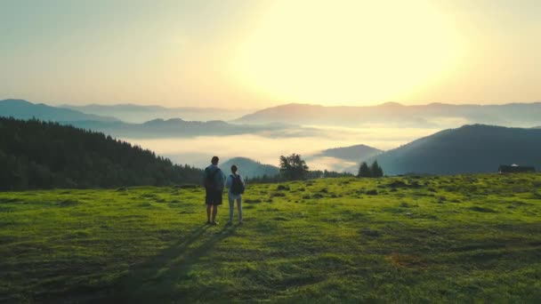 Man and woman meet the sunrise on top of the mountain. Aerial photography over their heads. The beauty of the Ukrainian Carpathians. Fabulous morning fog in a mountain valley — Stock Video