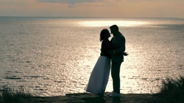 Silhouette eines Jungen und eines Mädchens, die sich vor dem Hintergrund des Meeres umarmen und küssen. Glückliches junges Paar traf sich bei Sonnenuntergang am Meer. Gemeinsam glücklich. — Stockvideo
