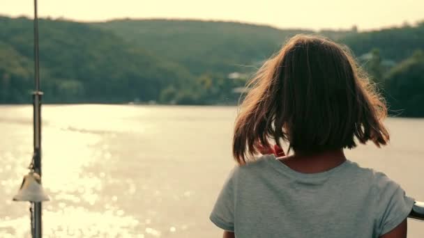 Silhuett av en tonårstjej som tittar in i fjärran med ryggen mot kameran. Flickan som tittar på havet slappnar av. — Stockvideo