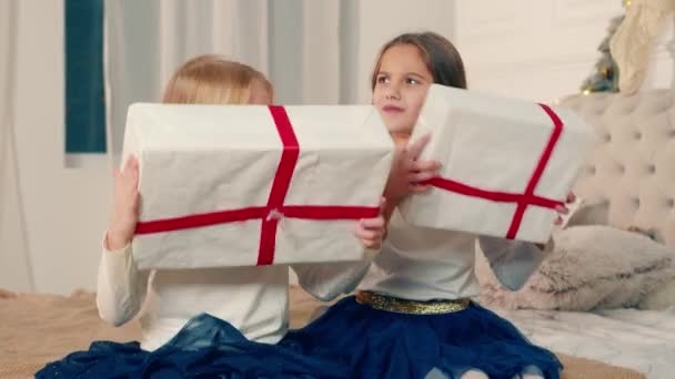 Dos niñas sosteniendo cajas de regalos de Navidad. Emociones felices de los niños sacudiendo cajas de regalo con la esperanza de averiguar lo que hay en la caja — Vídeos de Stock