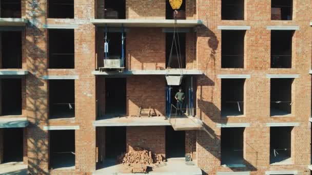 Costruzione di una casa di mattoni. Il costruttore prende il cemento dalla gru di costruzione. — Video Stock