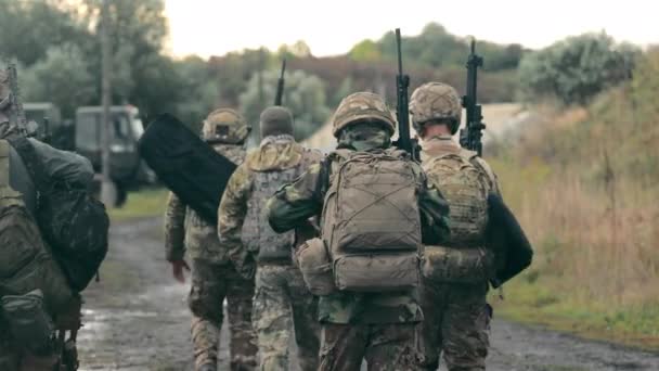 Un gruppo di militari di ritorno dopo aver completato un compito. Soldati in uniforme militare con mitragliatrici camminano su una strada pietrosa con le spalle alla cella. — Video Stock