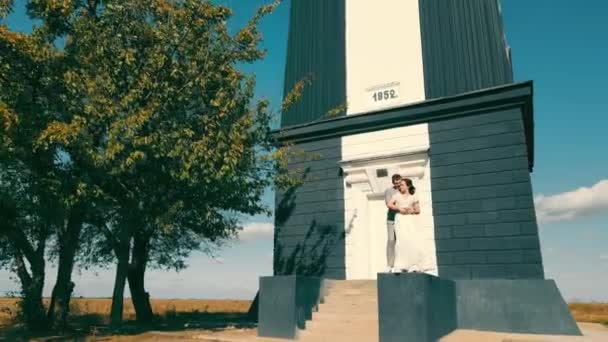Šťastný zamilovaný pár stojí blízko malé budovy na poli. Útulné místo pro dva lidi. Slunečný jasný den a dva milenci spolu. — Stock video