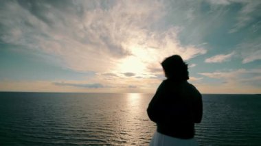 Denizin arka planında bir kadının silueti. Denizde gün batımına bakıp geleceği hayal eden bir kadın..