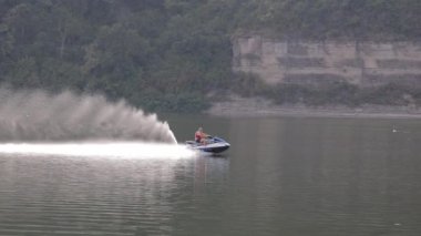 Yazın su eğlencesi. Bir adam nehirde jet ski sürüyor. Su motosikletinin yavaş çekimleri. Mobiletlerden büyük su sıçraması..