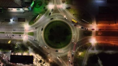 Gece bir kavşakta dönen arabaların hava trafiği. Gece şehri ve araba trafiği daire çiziyor..