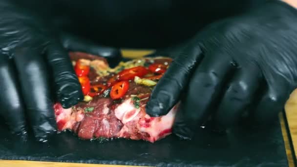 Gotować marynaty mięsa z warzywami. Ręce szefa kuchni w czarnych rękawiczkach sho mieszają kawałki warzyw i marynatę ze stekiem. Marynuję stek. Szef kuchni przygotowuje mięso.. — Wideo stockowe