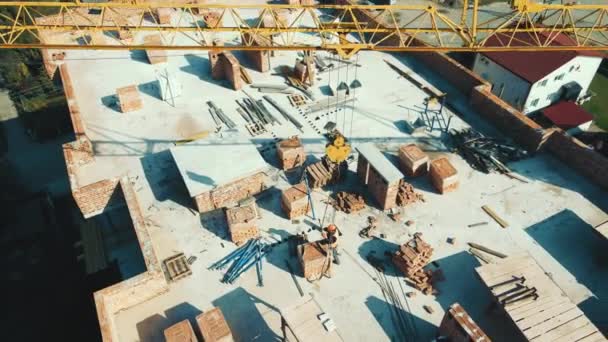 Aereo costruttore vista dall'alto sul tetto della casa attacca un pallet di mattoni per il sollevamento con una gru di costruzione. Costruire una casa con una gru da costruzione. — Video Stock