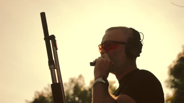 En mann med et våpen i hendene ved solnedgang røyker en sigar og lader om våpenet. Silhuett av en pilmann på bakgrunn av solen. – stockvideo
