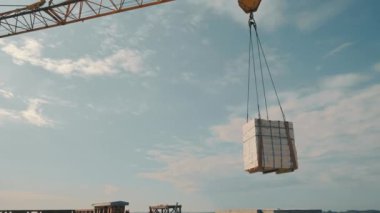 İnşaat vinci beyaz tuğlayı kaldırır ve inşaat alanına aktarır. İnşaat alanındaki bir vinç yük kaldırır..