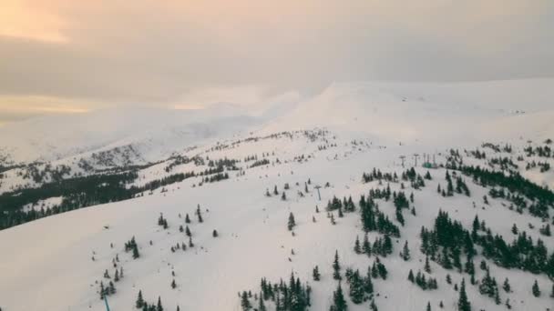 Alpy europejskie pokryte są śniegiem. Lot nad górskimi krajobrazami i choinkami pokrytymi śniegiem. Wieczorne kolorowe słońce oświetla żółte niebo. — Wideo stockowe