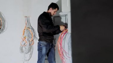 An electrical engineer connects an electrical switchboard in a new home. The man adjusts the electrical panel and arranges the electrical wires.