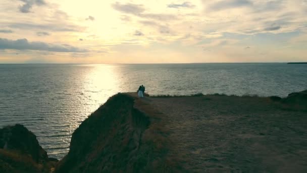 Duas pessoas felizes a caminhar para o mar à beira de um penhasco alto. As pessoas apaixonadas vão a um lugar romântico junto ao oceano — Vídeo de Stock