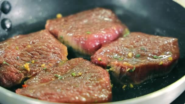 Čtyři kousky steaku jsou smažené na pánvi. Vařit steaky doma na pánvi. Šéfkuchař míchá kousky steaku na pánvi. — Stock video