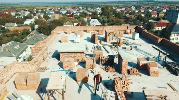 Evin çatısındaki havadan görüşlü inşaatçı inşaat vinci ile kaldırmak için tuğla paleti takıyor. İnşaat vinci olan bir ev inşa etmek.. — Stok video
