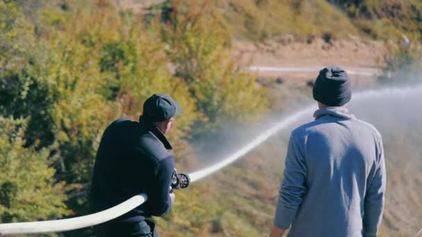 Två män håller en brandslang och vattnar objektet under högt tryck. En brandman släcker en brand.. — Stockvideo