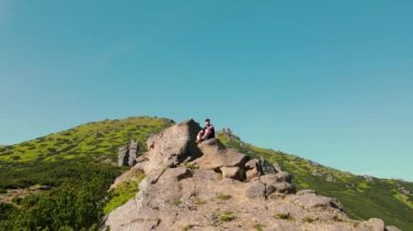 Genç bir erkek, bir dağın tepesinde oturuyordu. Bir uçurumun kenarında oturan yürüyüşçü, uzaklığa bakıyor. Geleceğe bakıyorum. Yürüyüşçü dağa tırmanırken dinleniyor.