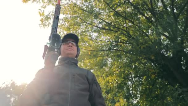 Porträtt av en manlig jägare med ett smoothbore jakt vapen i händerna på hörlurar och glasögon. — Stockvideo