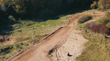 Motosikletlilerin üstündeki hava manzarası bir motokros yarışında keskin bir dönüş yapıyor. Dik virajları ve sıçrama tahtaları olan off-road motokrosları.