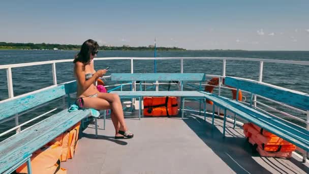 Een eenzame vrouw in een badpak vaart op een passagiersschip en surft op reis door een mobiele telefoon. Passagiersveerboot met één vrouw. — Stockvideo