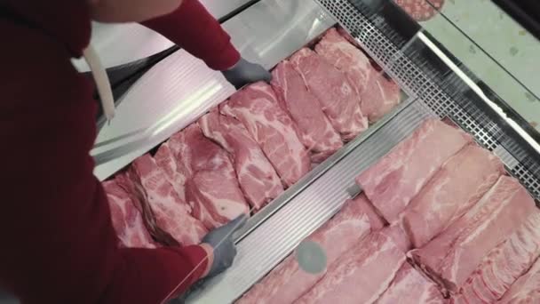 Le vendeur dans le magasin expose les produits de viande crue de près. Le vendeur met un plateau en métal avec de la viande crue sur la vitrine. — Video