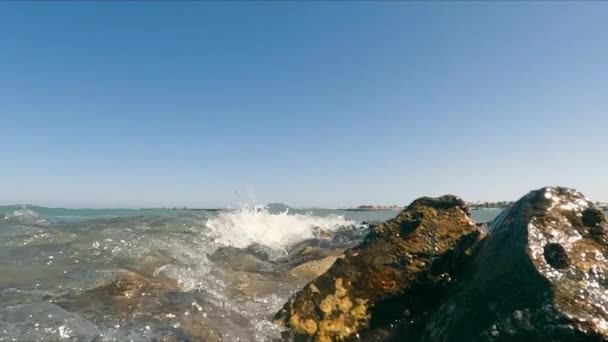 Крупный план морских волн, падающих на прибрежные скалы в безоблачный солнечный день. Медленное движение пузырящихся волн, катящихся по скалистому берегу с ясным синим небом на заднем плане, копирующее пространство. Концепция морского пейзажа — стоковое видео